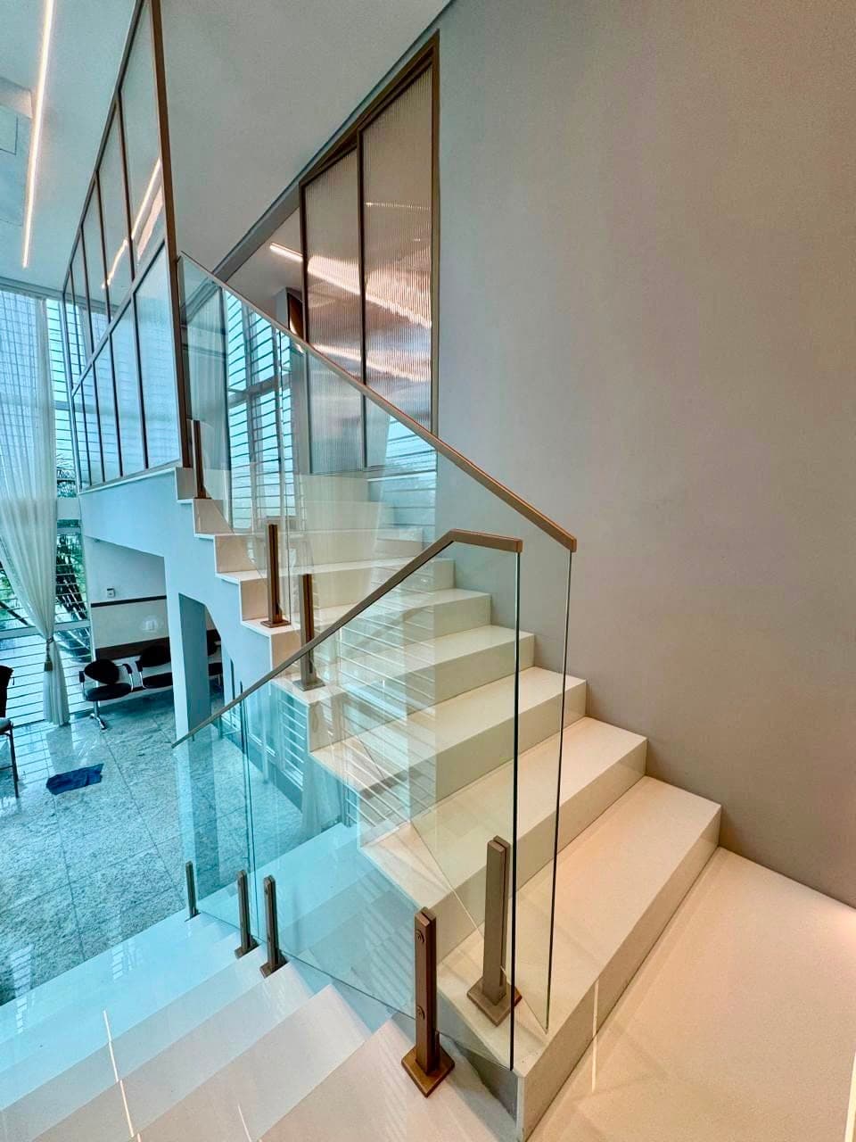 Escada com guarda-corpo de vidro e detalhes em bronze